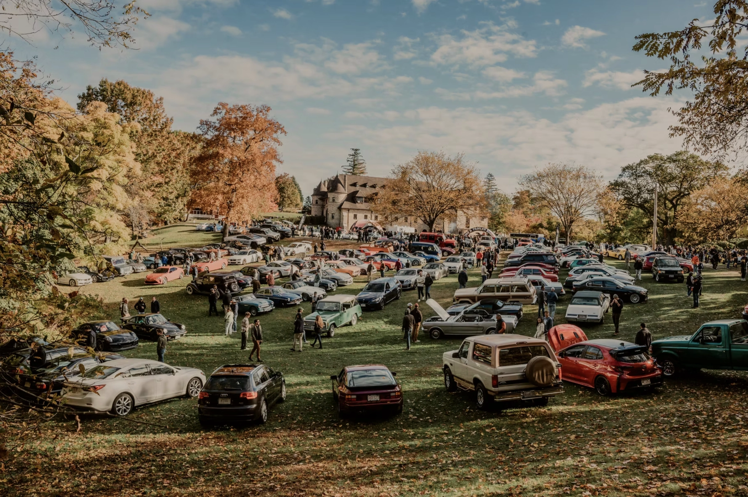 An autumn gathering of motorcars across the museum grounds, surrounded by trees in fall color
