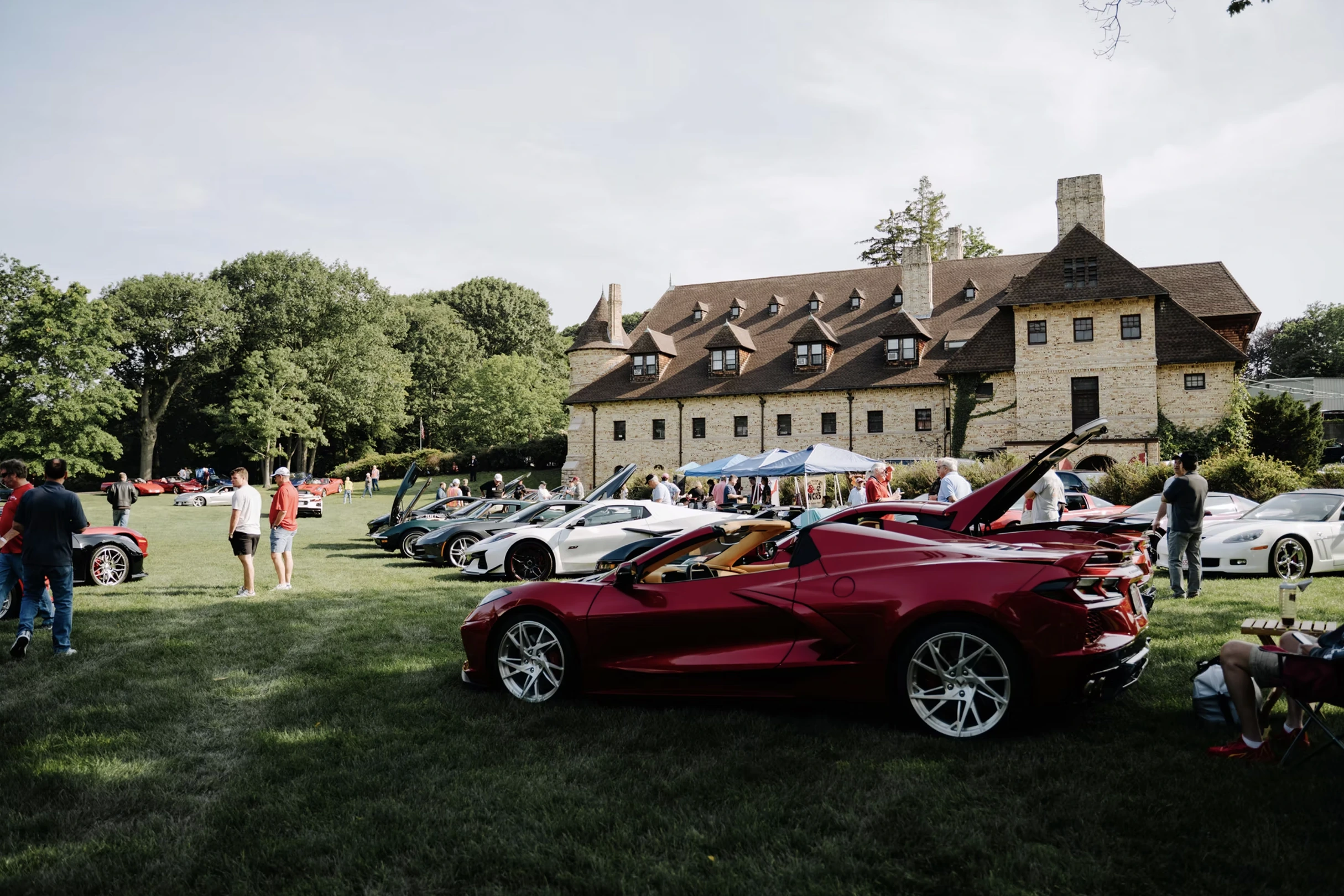 A burgundy sports car and a gathering of automobiles on the Larz Anderson Museum grounds