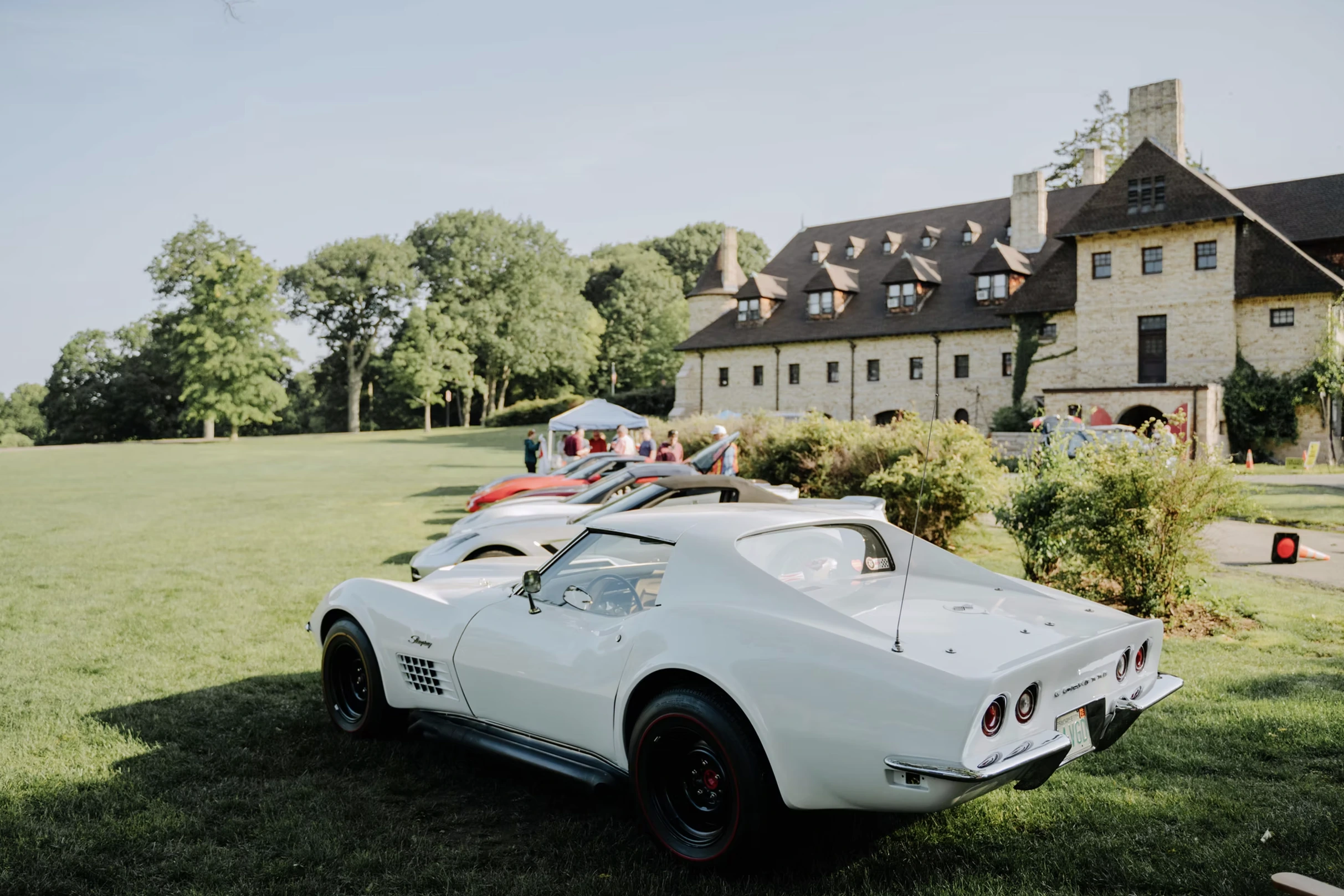 A white vintage Corvette among motorcars on the lawn beside the carriage house
